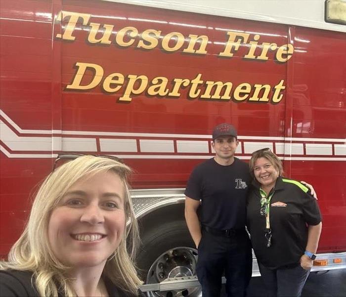 Three people posing in front of a fire truck.